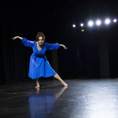 Katja Köngäs dansar i en blå klänning mot en svart bakgrund. 