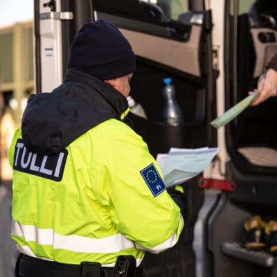 En lastbilschaufför räcker dokument till tullens tjänsteman i overall.