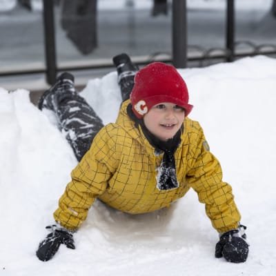 Ekaluokkalainen Ilya Skurnik makaa mahallaan lumessa käsiin nojaten ja katsoo eteenpäin. 
