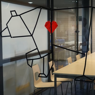 Tomma stolar vid ett långt bord bakom en glasvägg som pryds av en bild på en björn med rött hjärta i Lagstads skola.
