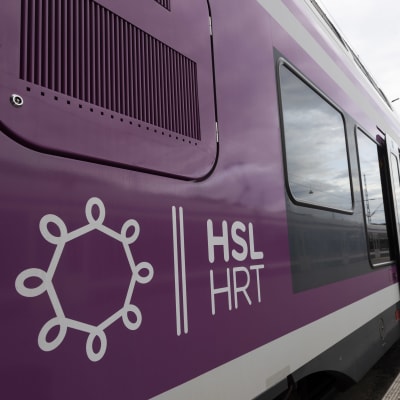 Valko-liila lähijuna pysähtyneenä laiturille. Kyljessä HSL/HRT logo.