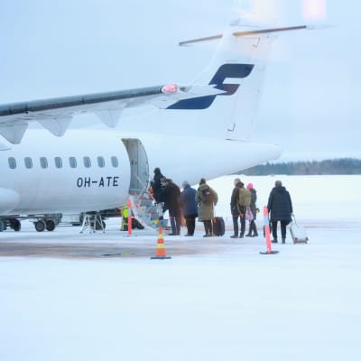 Matkustajia nousemassa lentokoneeseen talviselta lentokentältä.