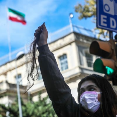 Mielenosoittaja pitelee hiustuppoa kädessään. Taustalla näkyy Iranin konsulaattirakennus.