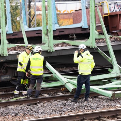 Kolme miestä seisoo junaradalla tarkastelemassa ratavauriota. Työtakkien selässä lukee Destia. 