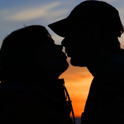 Man och kvinna kysser varandra framför solnedgång