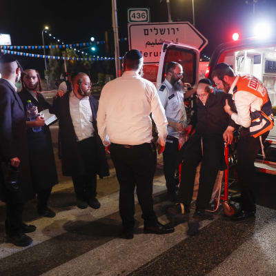 Två personer hjälper en tredje vid en ambulans till höger. Till vänster fyra personer till.