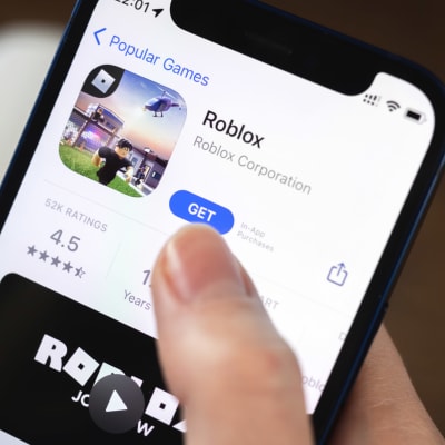En smarttelefonskärm som visar speler Roblox i appbutiken, med en hand som håller i telefonen.