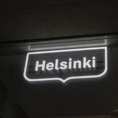 Helsingfors stads logotyp som neonskylt på en vägg i mörkret.