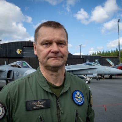 Juha-Pekka Keränen katsoo vakavana kameraan. Taustalla näkyy eri merkkisiä hävittäjälentokoneita.