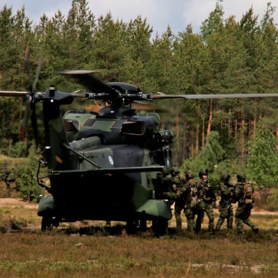 En militär transporthelikopter har landat i en glänta, en grupp soldater stiger på.