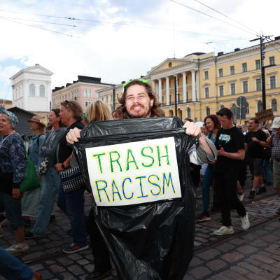 Demonstranten Paul Nix med en soppåse med en skylt där det står skrivet: TRASH RACISM