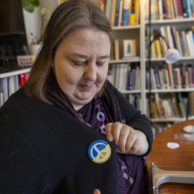 Kvinna fäster på sin tröja en pins med fredssymbol.