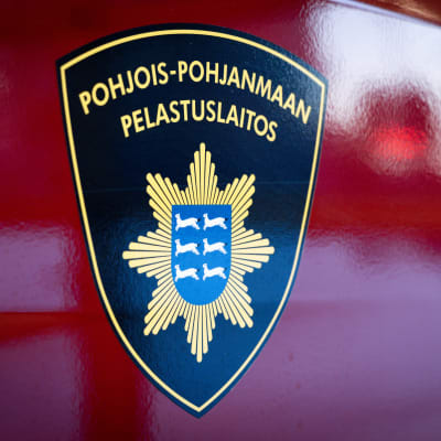 Pohjois-Pohjanmaan pelastuslaitoksen logo hihassa ja palo-autojen kyljessä.