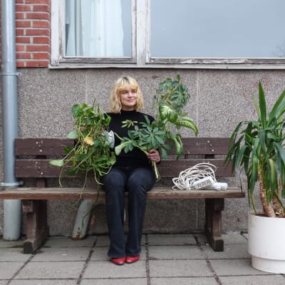 Tia Hassinen sitter på en bänk utanför Strömborgska skolan, med två plantor i handen.