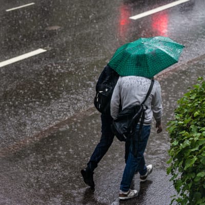 Kaksi ihmistä kävelee yhden sateenvarjon suojassa rankkasateessa.