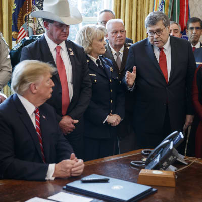 President Trump sittande vid skrivbord, med folk omkring sig, bla jusititieminister Barr och man med stor cowboyhatt.