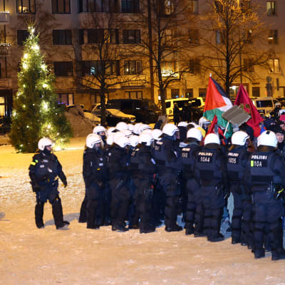 Ett stort antal kravallpoliser pressar en grupp demonstranter från Tölö torg i Helsingfors. En julgran står tänd på det snöklädda torget.