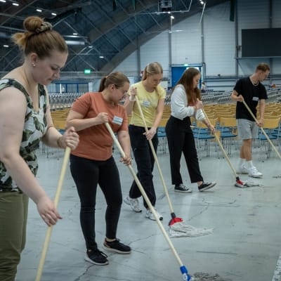 Vapaehtoiset nuoret siivoavat salin lattiaa
