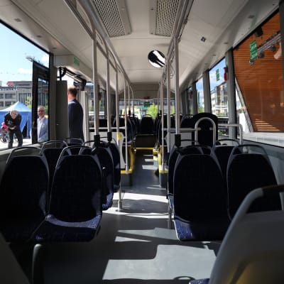 Kuvassa on uuden sähköbussin käytävä. Bussin ikkunoista näkyy aurinkoinen Joensuun kauppatori.