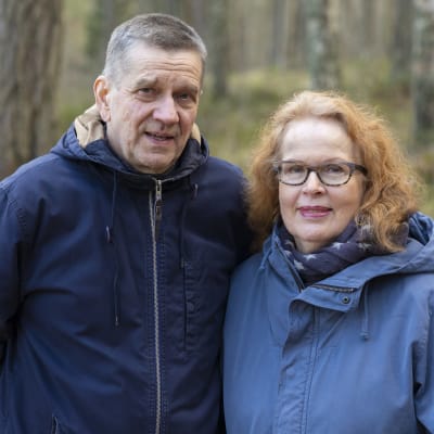 Olli (vas.) ja Riitta Jalonen seisovat metsässä vierekkäin ja katsovat kameraan.