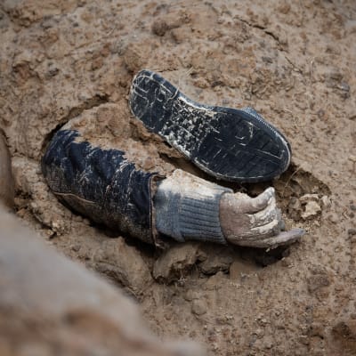 En arm och en sko halvt begravda i sand.