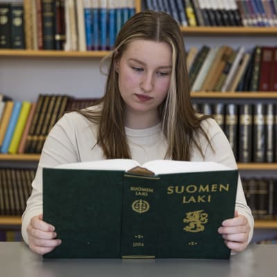 Kemiläinen abiturientti Sara Ylimäki istuu pöydän ääressä ja lukee Suomen laki -kirjaa koulun kirjastossa. 