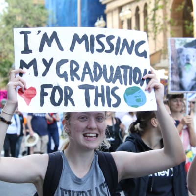 En klimataktivist håller upp ett plakat med texten "Im missing my graduation for this".