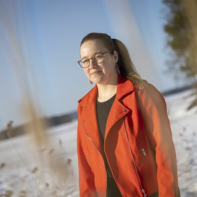 Paula Wegelius katsoo maisemaa Kuopiossa. Taustalla heinää ja jäätynyt järvimaisema.