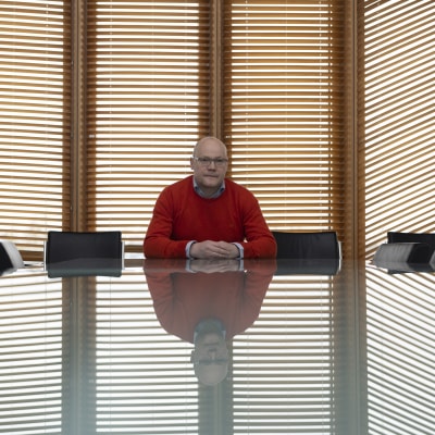 Elintarvikemarkkinavaltuutettu Olli Wikberg istuu tyhjän neuvottelupöydän ääressä ja katsoo suoraan kameraan.