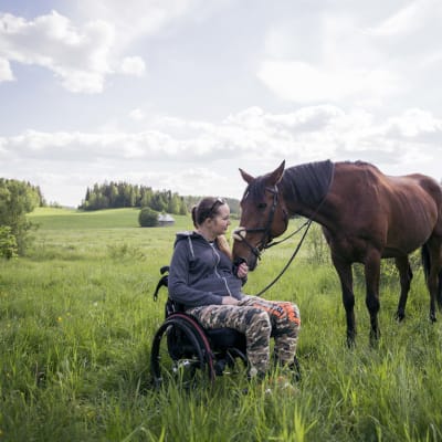 Nicole Hellberg sitter i sin rullstol ute i hagen med sin häst.