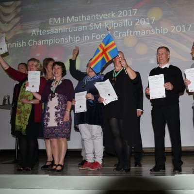 Flera personer står på en scen efter att de fått medaljer i mattävlingen Mathantverk.