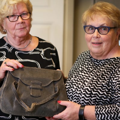 Aira Hellström och Marja-Leena Suvitie, två damer med glasögon, håller i en större, brun handväska.