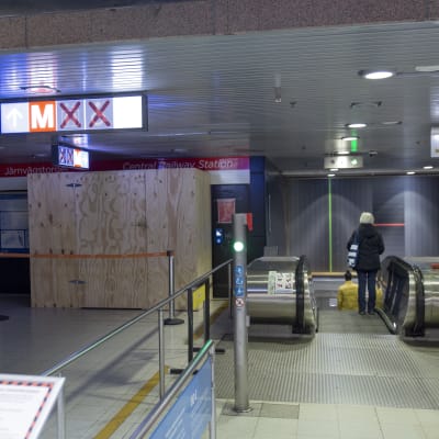 Punaisella ruksilla merkityt pyörätuoli- ja hissiopasteet sekä työmaa-alueen lautaseinä Helsingin päärautatieaseman metroasemalla.