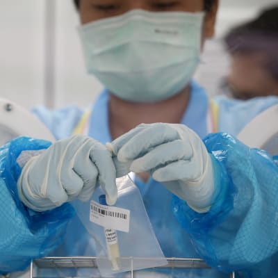 En person i skyddsutrustning håller i ett coronavirus-provsvar.