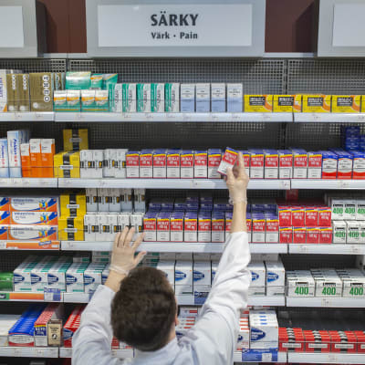En apotekare fyller hyllorna med smärtstillande mediciner. 