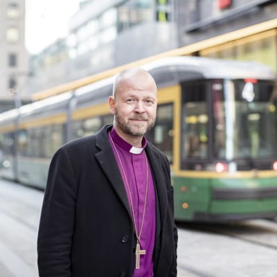 Piispa Teemu Laajasalo seisoo Helsingin keskustassa raitiovaunun edessä.