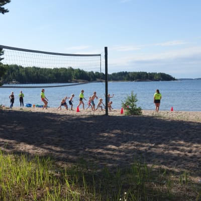 Simskoledeltagare leker på stranden med en volleybollsplan i förgrunden.