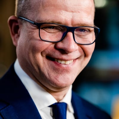 En leende man i närbild med blåa glasögonbågar och blå kostym.