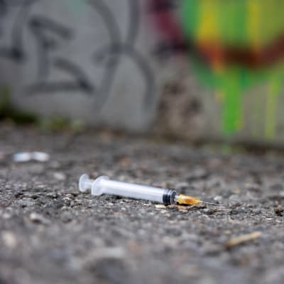 En använd injektionsspruta ligger på asfalten. 