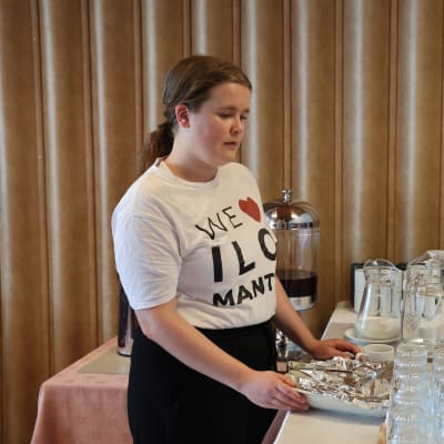 Työharjoittelija Milla Turpiainen siivoaa hotellin aamiaispöytää. 