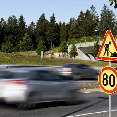 Bilar kör förbi trafikskylt. Skylten visar en hastighetsbegränsning på 80 kilometer per timme.