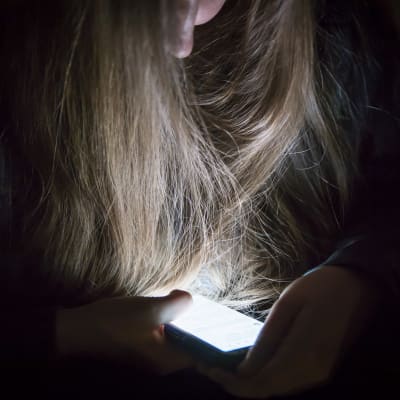 En flicka med långt hår sitter med en mobil i handen. 