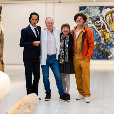 Nick Cave, Thomas Houseago och Brad Pitt tillsammans med en fjärde person, en anhörig till Houseago, på Sara Hildéns konstmuseum. De står och håller om varandra och och omkring dem skymtar skulpturer och på väggen bakom dem en målning.