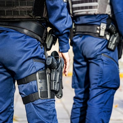 Två poliser, fotade bakifrån. En av poliserna har ett vapen i hölster.