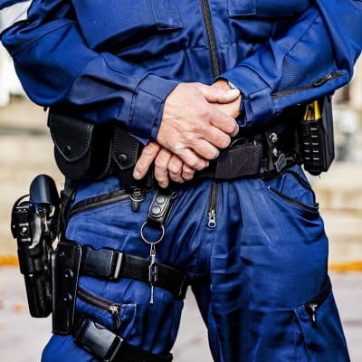 Närbild av en polis som står med händerna i kors över magen.