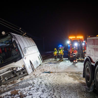 Lumisella tiellä kyljelleen kaatunut linja-auto ja pelastuslaitoksen työntekijöitä.