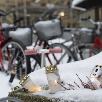 Hautakynttilöitä lumessa Ullanlinnan surmapaikan edessä 18. joulukuuta. Taustalla luminen piha ja polkupyöriä.