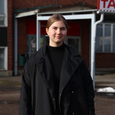 En ung kvinna står framför en skolbyggnad.