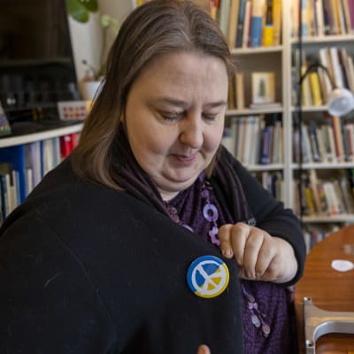 Kvinna fäster på sin tröja en pins med fredssymbol.