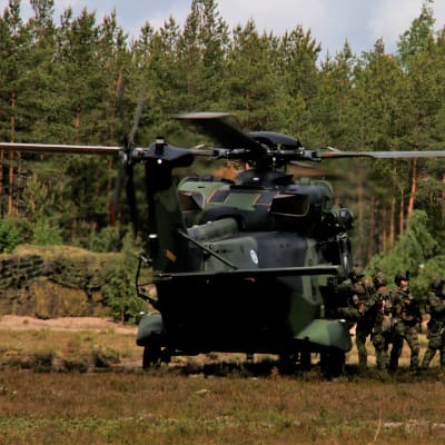 En militär transporthelikopter har landat i en glänta, en grupp soldater stiger på.